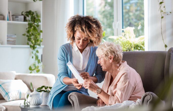 Female home caregiver supporting senior woman in her house, explaining her documents.
